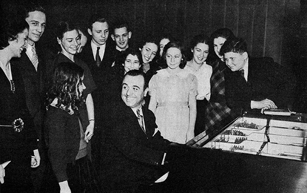 man at piano with students gathered around