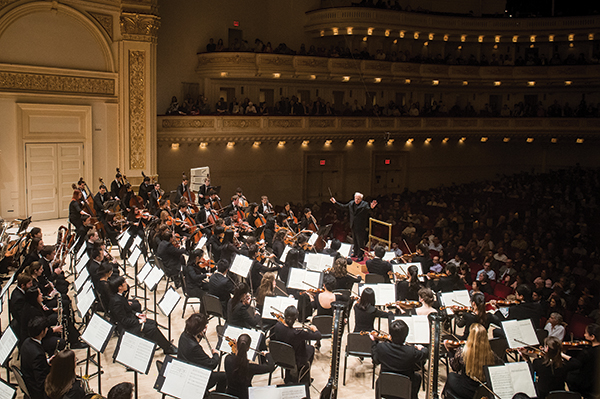 orchestra on stage at carnegie hall conducted by man