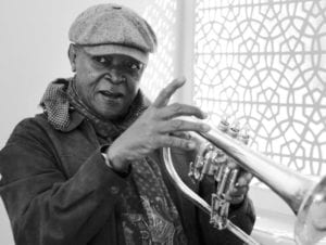 Hugh Masekela, reknowned South African trumpeter, singer and activist, with a jacket, scarf, and cap holding a flugelhorn