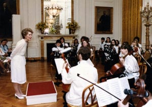 woman in white dress speaks to orchestra